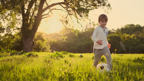 Happy-boy-running-with-soccer-ball-running-at-sunset-in-summer-field.